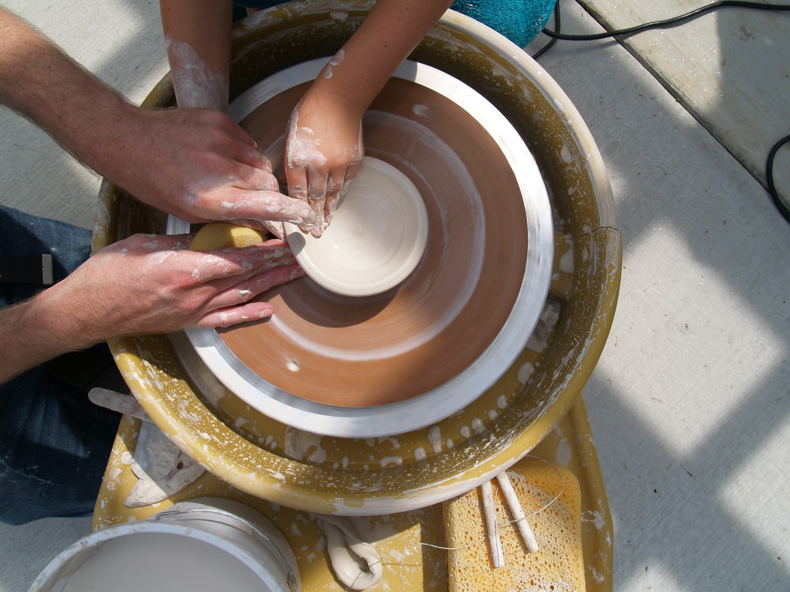 Two people shaping clay together at a pottery wheel